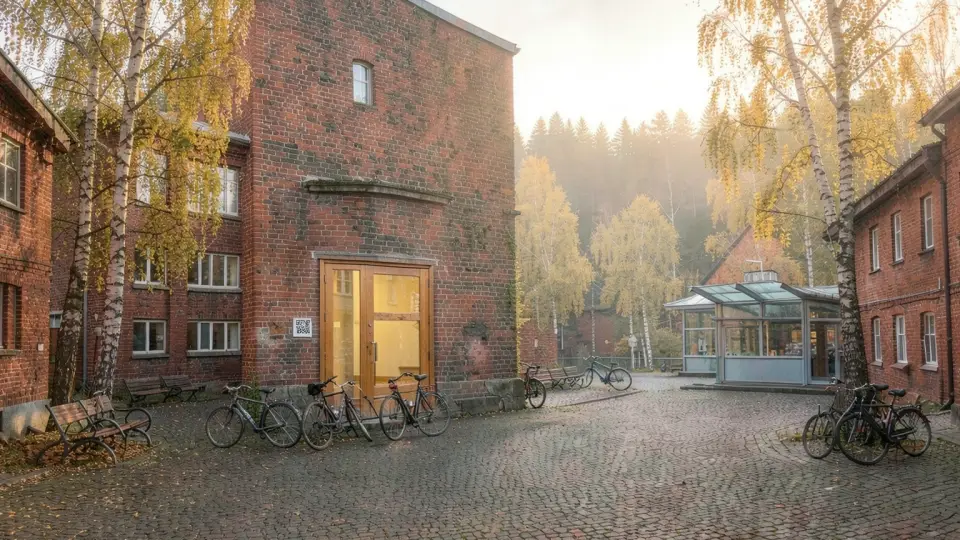 AI-genererad bild av Källan utifrån: ett rödbrunt tegelhus i två våningar med glasdörr och cyklar vid trappan.